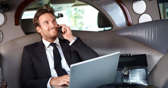 Man in business suit holding laptop sitting inside limousine